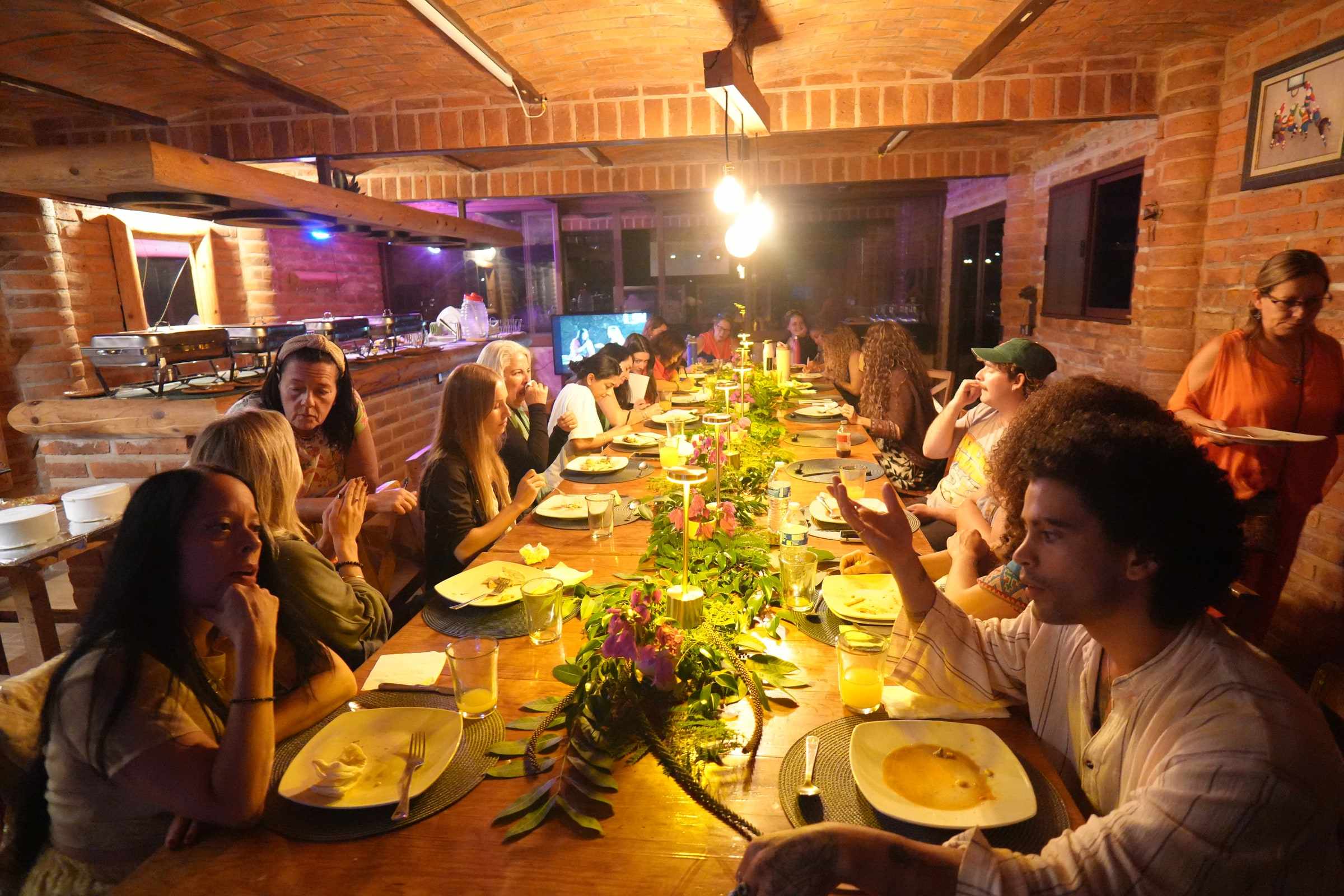 Guests sharing dinner at a long table in warm light