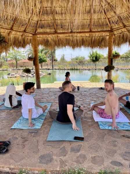 Guests sitting on yoga mats under the palapa by the lake