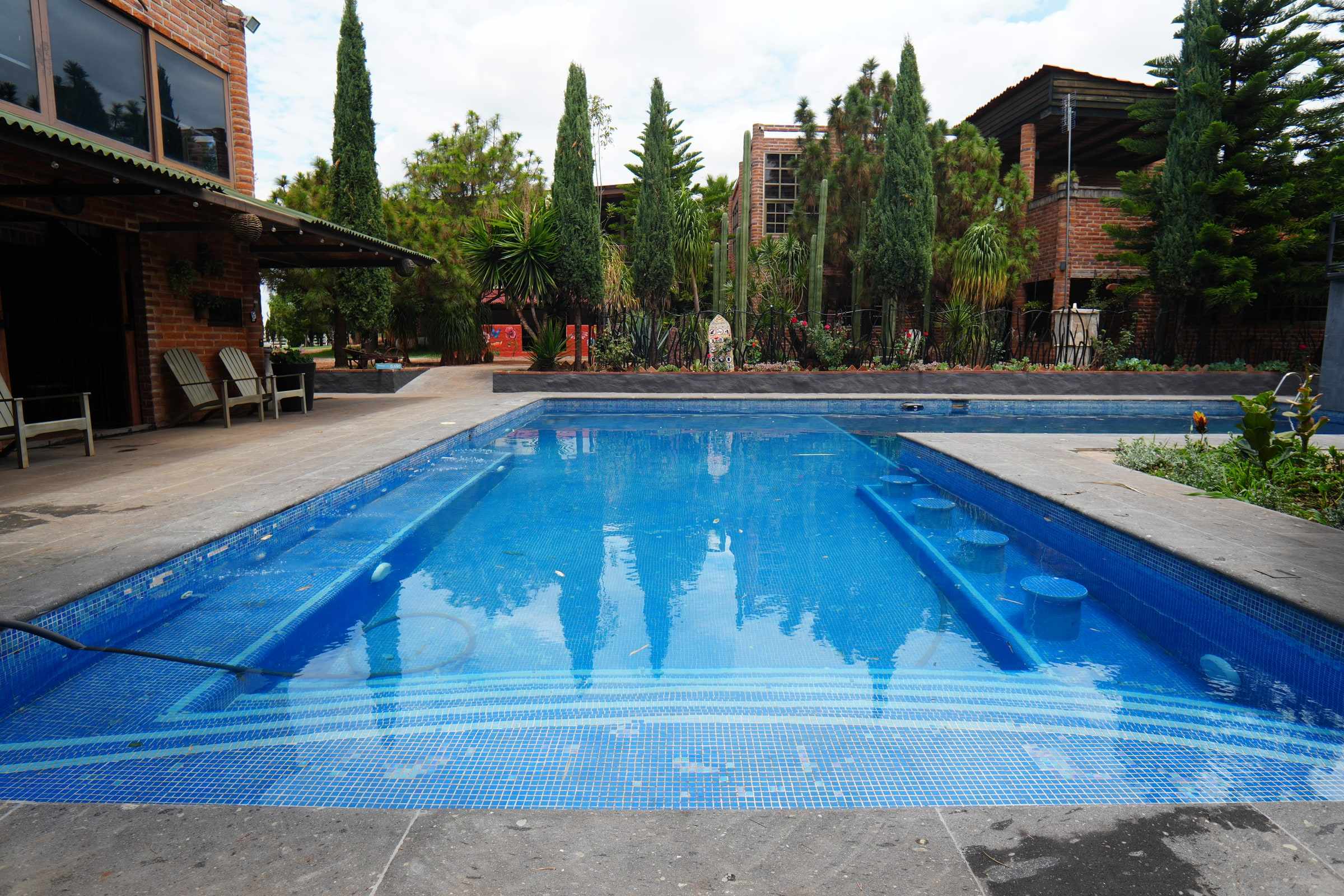 The long pool with cypress trees and brick buildings behind