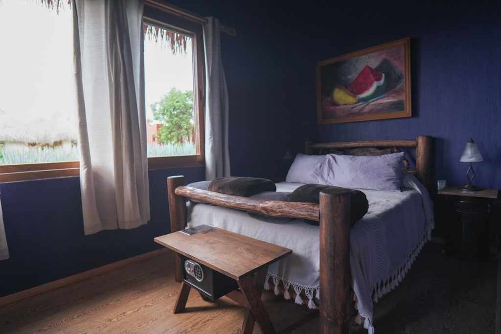 Tilopa, a deep blue room with a log bed and a window onto the agave